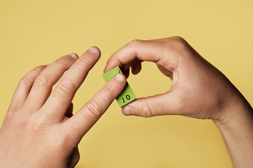 A child's hands hold a green LEGO Braille Brick with raised bumps representing the letter J