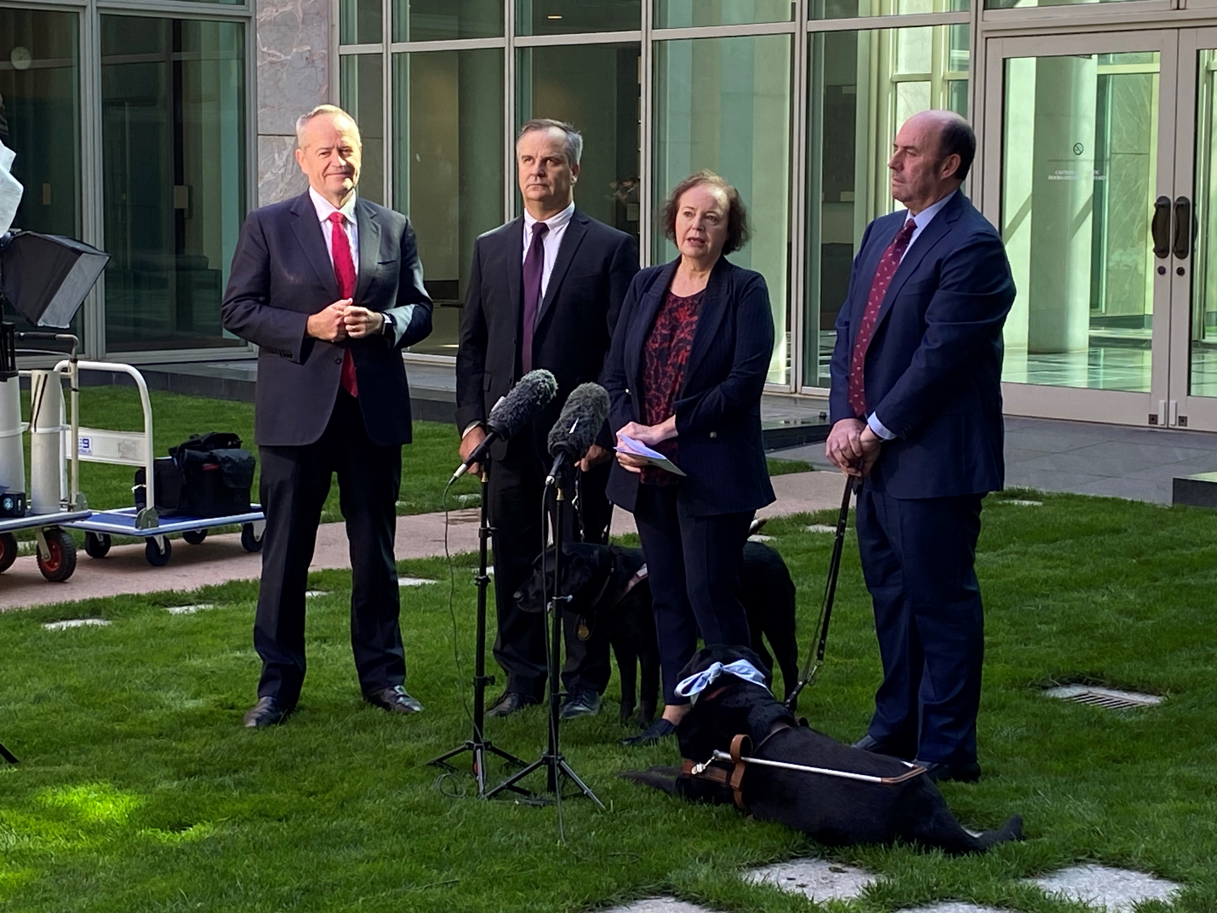 Two men and woman stand at microphones in a courtyard