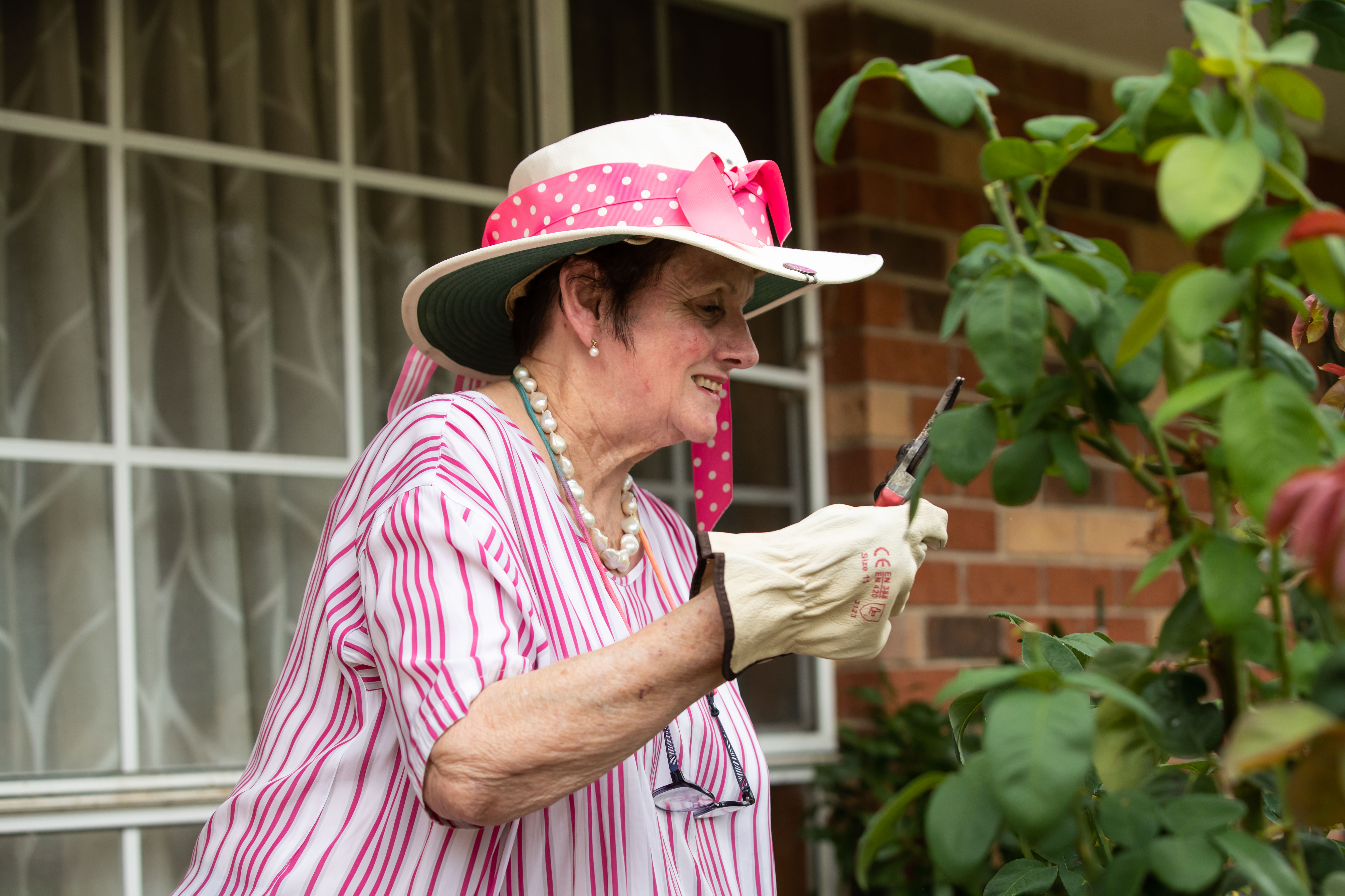 "A woman holding secateurs and smiling while tending to her garden."