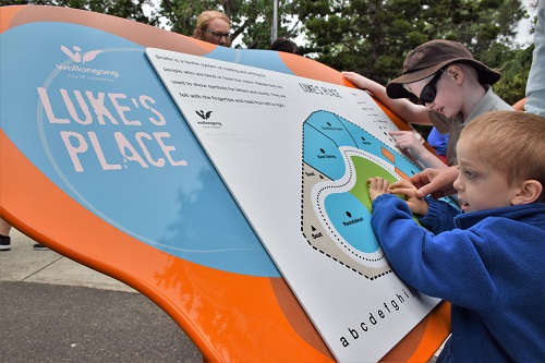 Two young boys use their hands to explore a braille sign