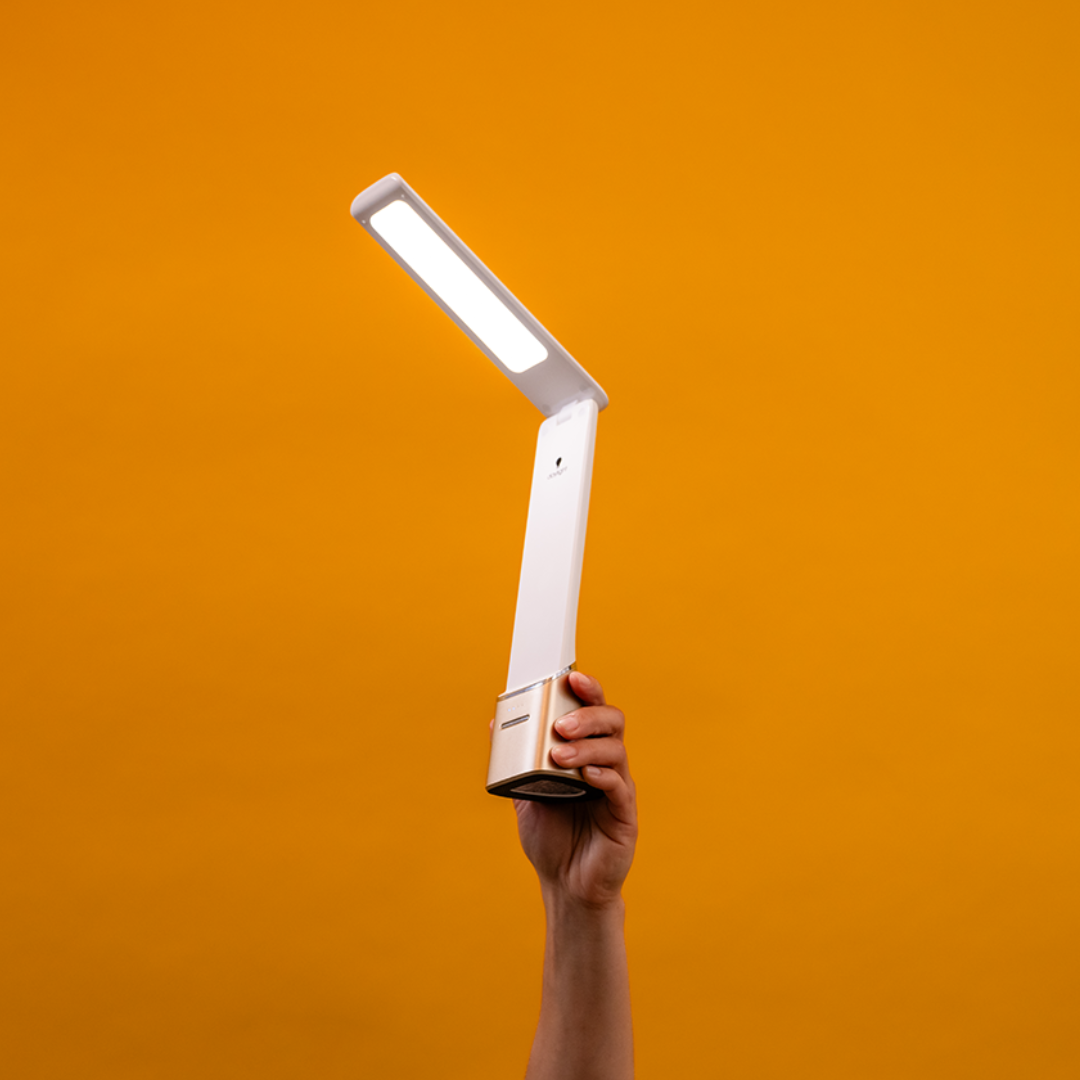 A person holds a modern portable lamp against an orange background.