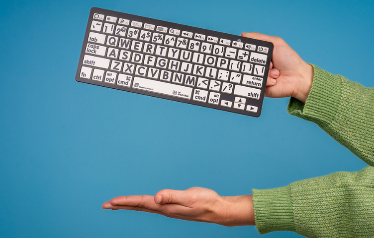 Someone wearing a green jumper holds a black-and-white high contrast keyboard in front of a blue background, mimicking the action of a film clapper board.