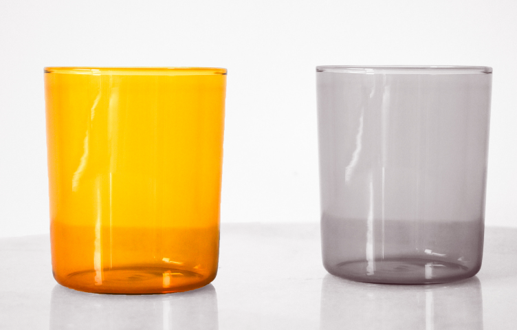 Two glasses sit atop a marble table. One glass is bright yellow to make it easier to see, while the other glass is clear to make it blend in.