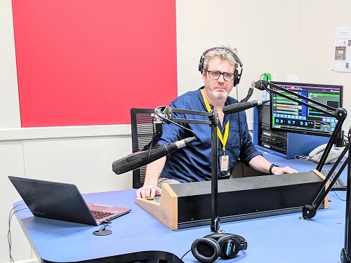 A man sits behind the control panel in a radio studio