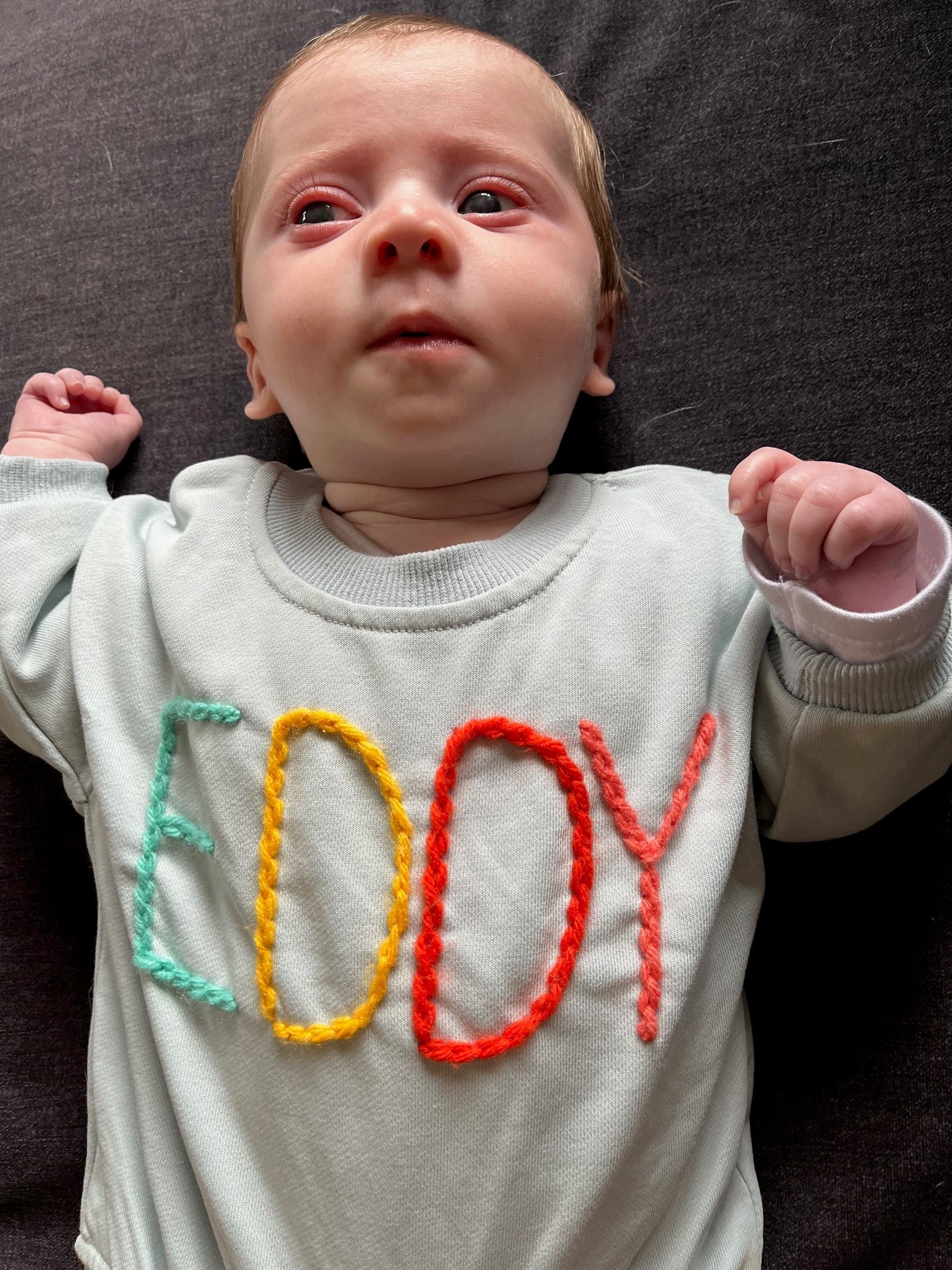 "Eddy lying on the ground wearing a shirt that has embroided letters reading EDDY."