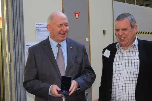 Two elderly gentlemen stand next to each other in a corridor