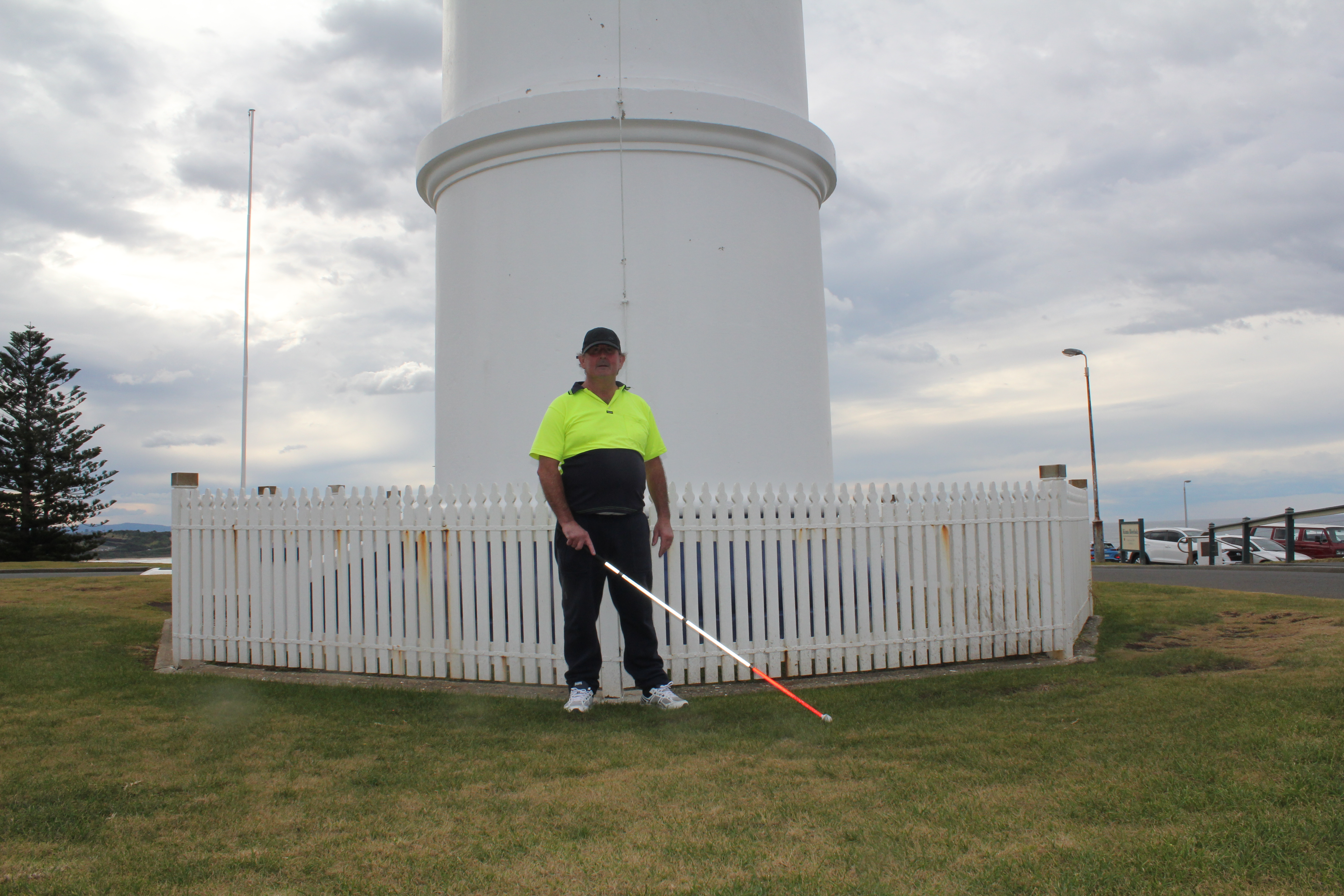 "David standing outside a tall white structure, white cane in hand."