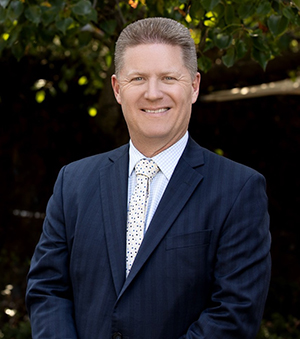 Vision Australia GM Fundraising, Marketing and Communications Ian Finlayson is smiling at the camera. He has short dark blond hair and is wearing a dark suit with a black and white polka dot tie