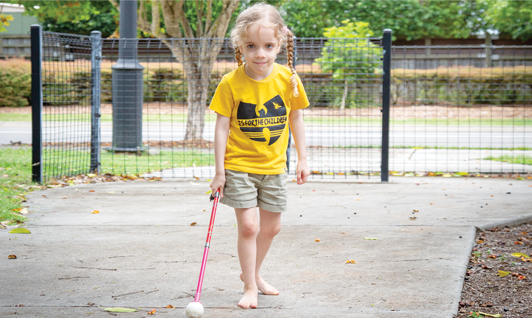 A young girl is walking along a footpath whilst holding a white cane