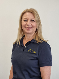 A woman with blonde shoulder-length hair and wearing a navy Vision Australia polo shirt smiles at the camera