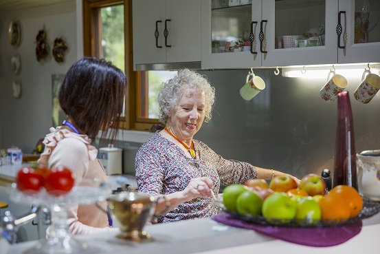 Two women standing in a kitchen, one cooking over a stove