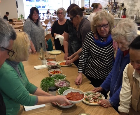 Group assembling pizzas in their final stages, adding toppings before they are cooked to enjoy