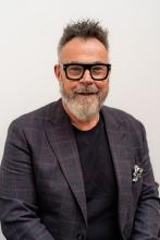 An image of Graeme Craig. He is wearing a dark grey blazer with a pocket square and looking into the camera.