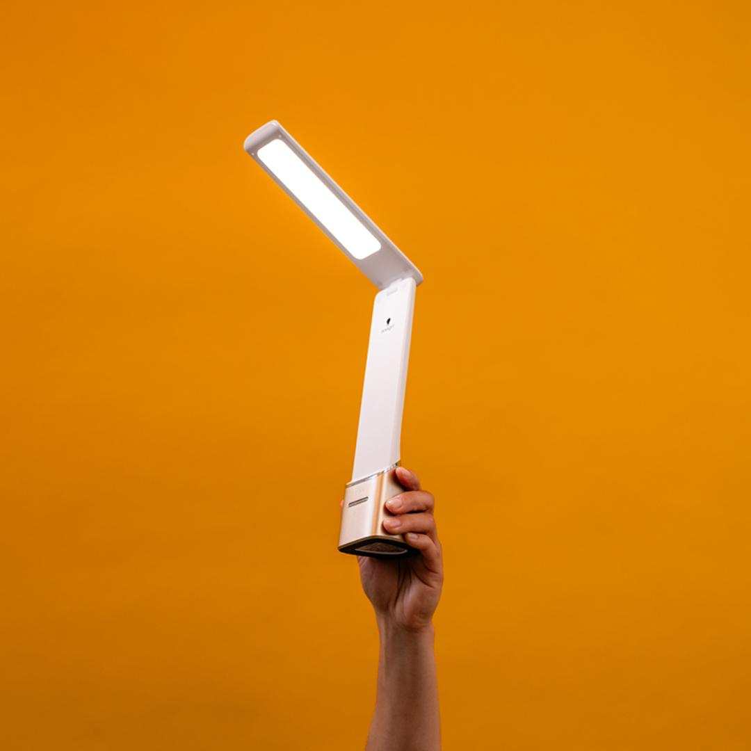 A person holds a modern portable lamp against an orange background.