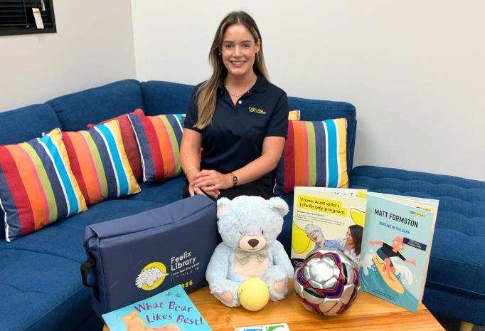 Kaylie is sitting on a blue couch, surrounded by toys and games she uses in her practice