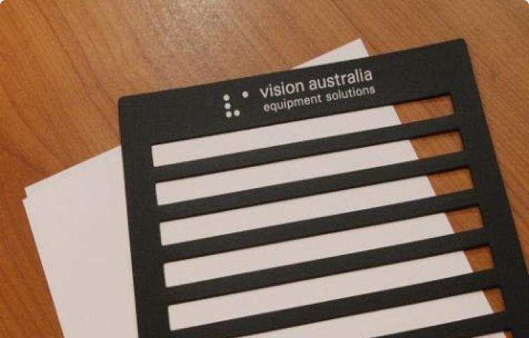 A black plastic writing guide with horizontal cutouts, labelled "Vision Australia Equipment Solutions.